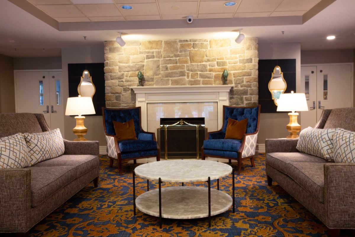 A cozy living room with sofas and armchairs arranged around a fireplace, accented by lamps and a round coffee table.
