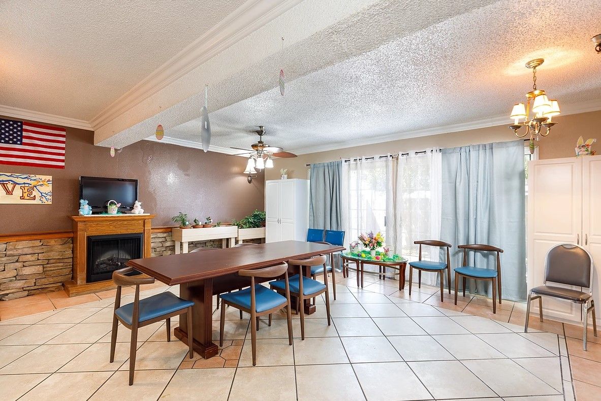 A spacious dining room featuring a large table with blue chairs, a fireplace, and large windows with curtains.