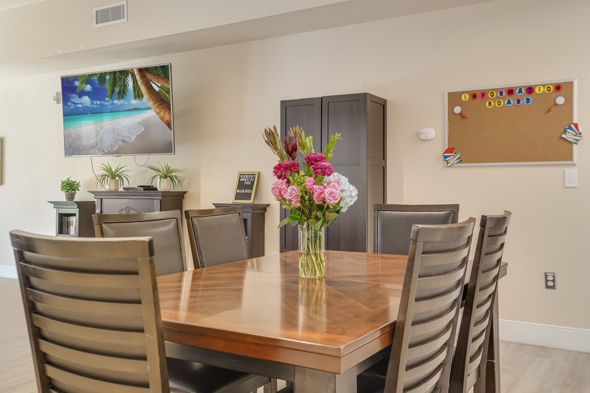A dining room with a wooden table, surrounded by chairs, and a vase of colorful flowers as the centerpiece.