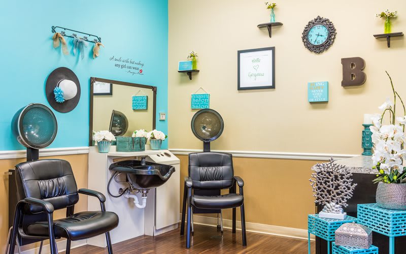 A cozy salon interior featuring a hair washing station, chairs, and decorative wall art in teal and beige tones.