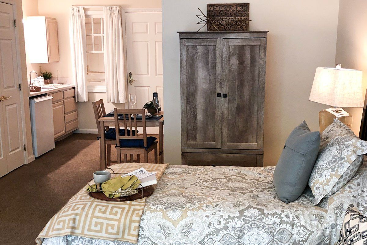 A cozy bedroom setup with a bed, wooden wardrobe, and dining area.