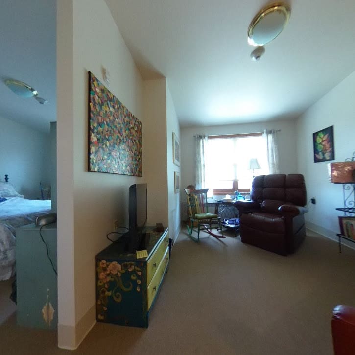 A cozy living space with an armchair, television, and a window allowing natural light in, adjacent to a bedroom.
