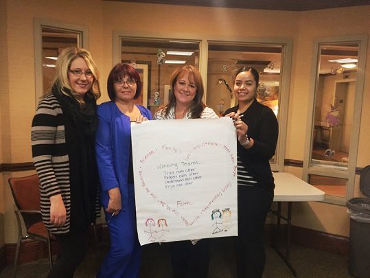 A group of women holding a poster with a heart drawn on it, standing indoors and smiling.