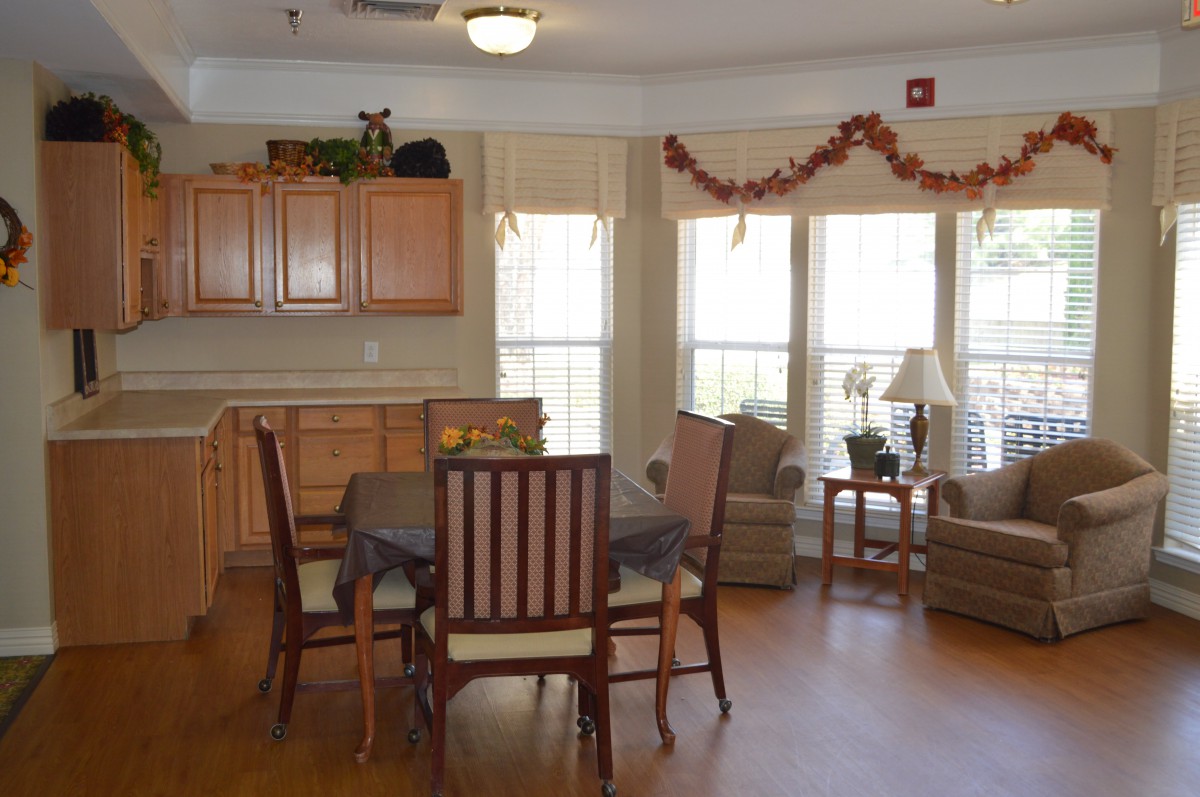 A cozy living and dining area with ample natural light, featuring a wooden table, chairs, comfortable seating, large windows, and warm decor.
