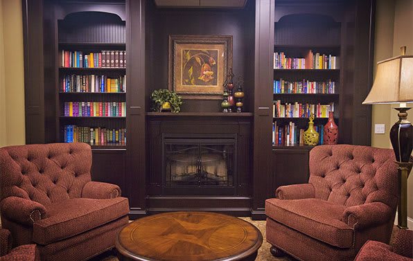 A cozy reading nook featuring bookshelves, armchairs, and a fireplace.
