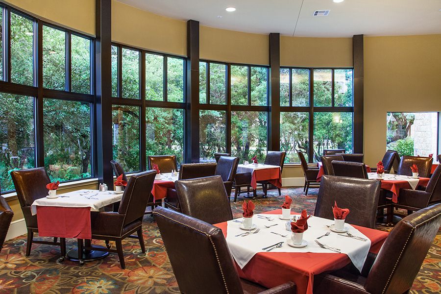 A spacious restaurant dining room with large windows and neatly set tables.