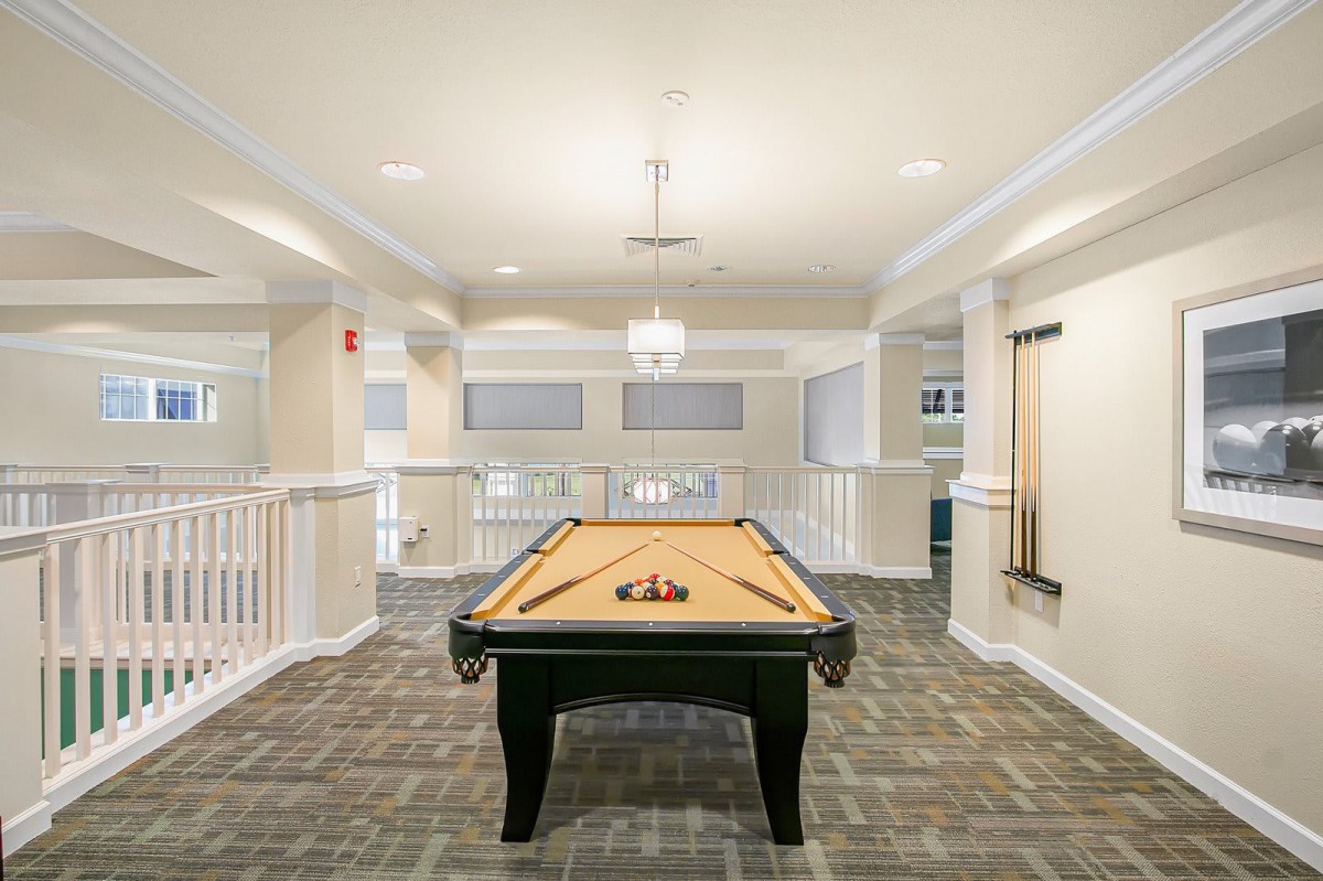 A modern recreation room featuring a pool table with carpeted flooring and elegant lighting.