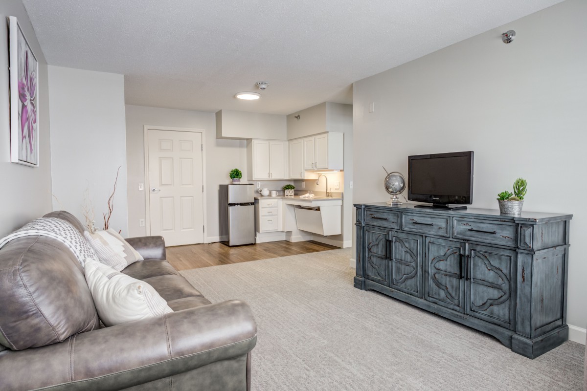 A modern living room connected to a kitchen area, featuring a sofa and a TV on a stylish cabinet.