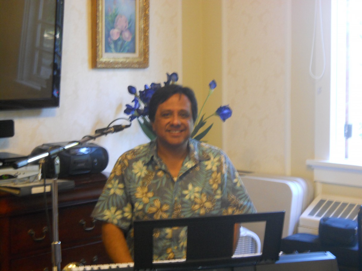 A person wearing a floral shirt sits indoors behind a keyboard.