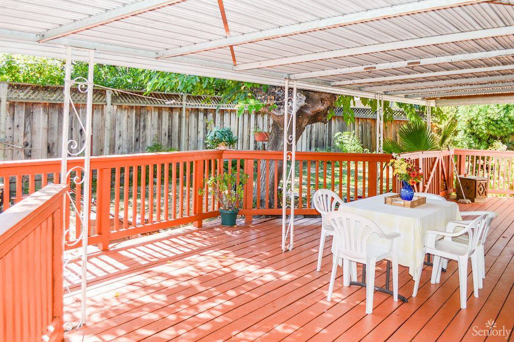 A spacious wooden deck with a table and chairs under a covered area, surrounded by a railing.