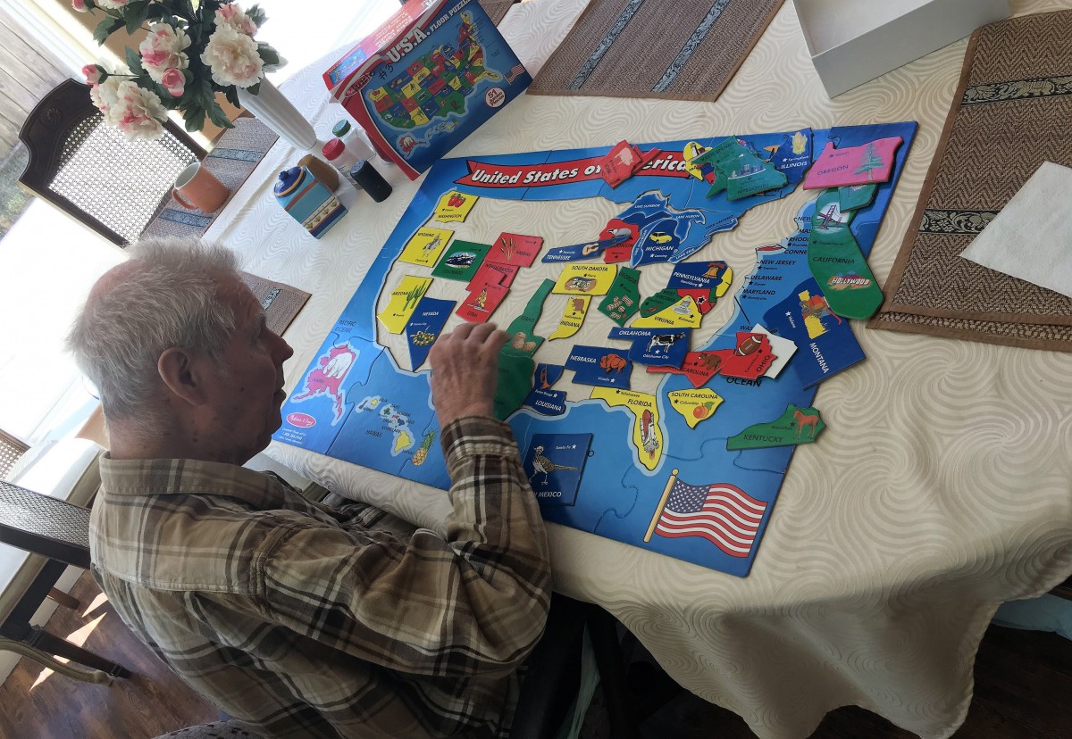 An elderly person working on a USA map puzzle at a table.