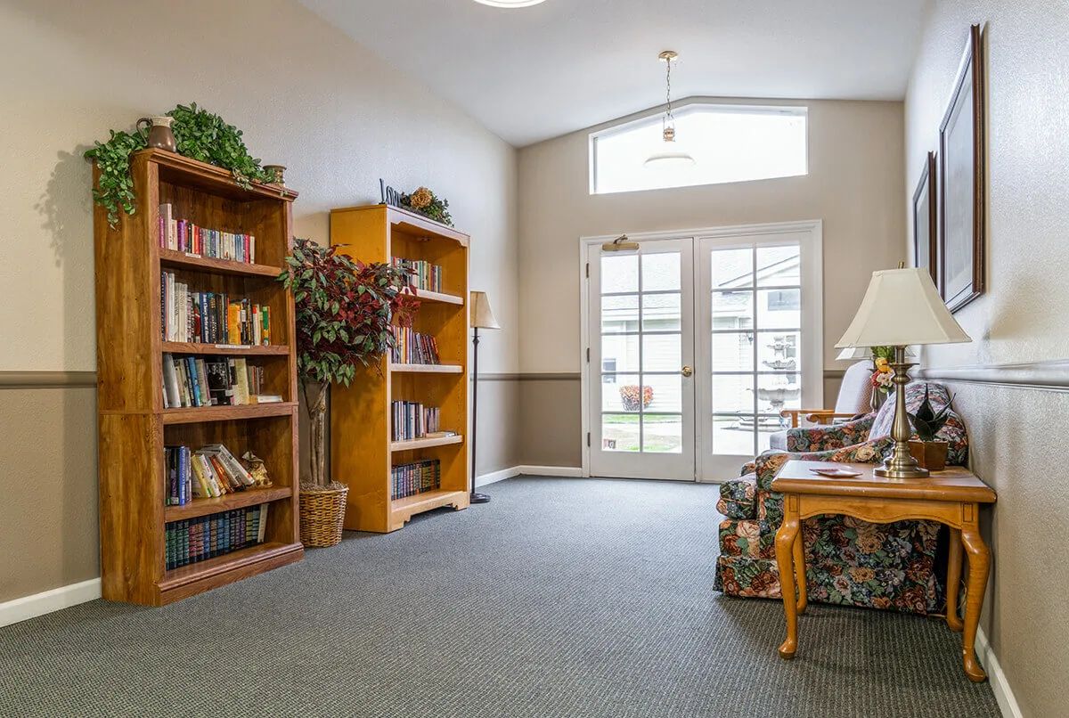 A cozy library corner with bookshelves and a comfortable seating area, illuminated by natural light from large windows.