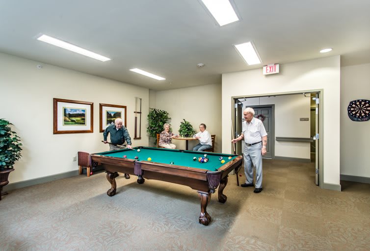 A group of seniors enjoying a game of billiards in a recreation room.