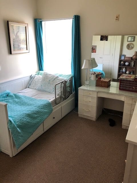 A cozy bedroom featuring a single bed with teal accents and a vanity desk with a mirror.