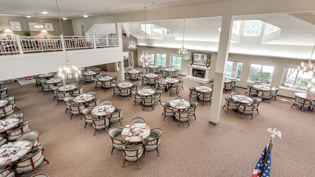 A spacious dining area with multiple round tables and chairs, set in a well-lit room with high ceilings.