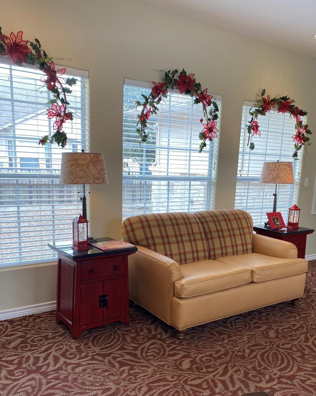 A cozy living room with a sofa, side tables, and floral decorations on the windows.