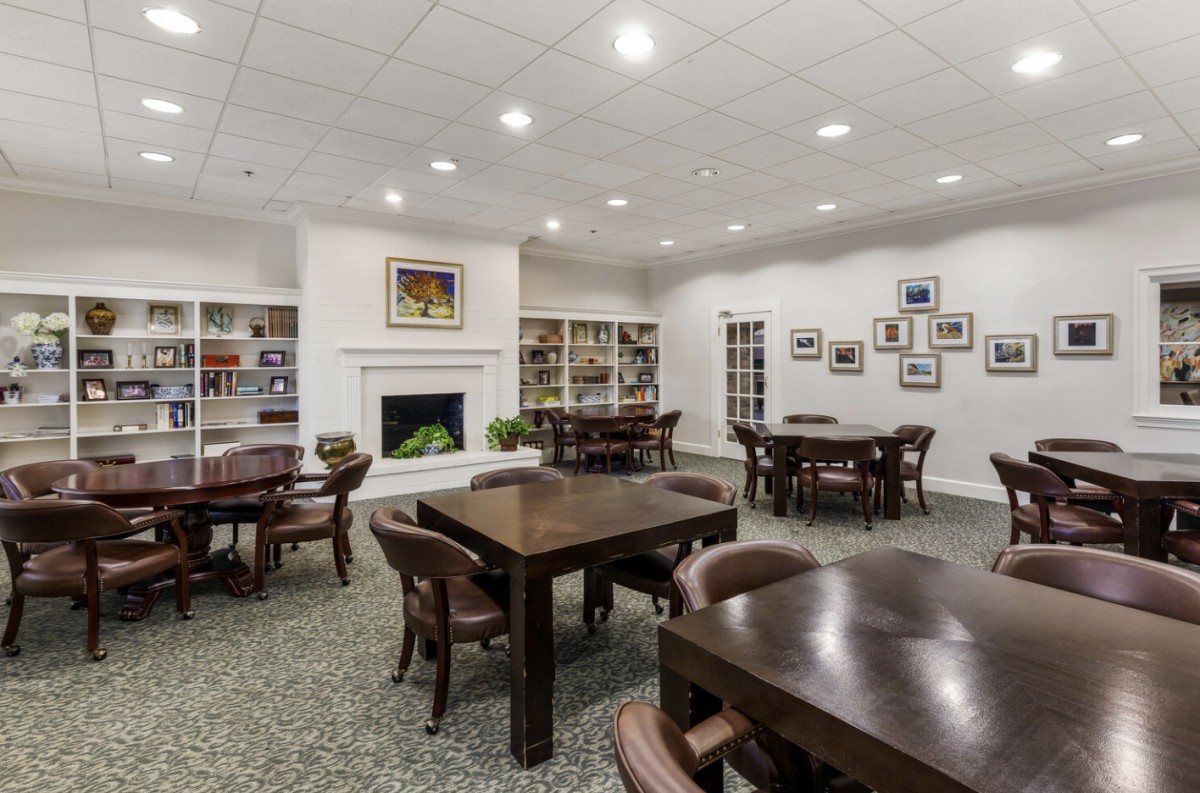 A spacious library reading room with tables, chairs, bookshelves, and a fireplace.