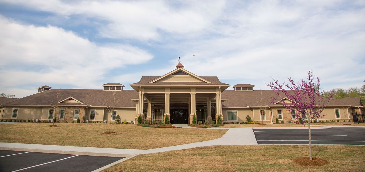 A large building with a grand entrance featuring columns and landscaped surroundings under a partly cloudy sky.