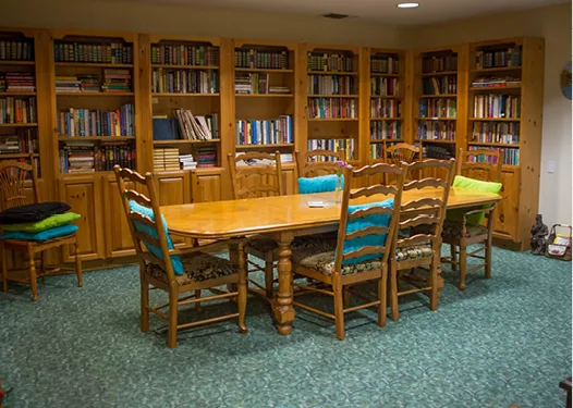 A cozy library room with a wooden table surrounded by chairs, and bookshelves filled with books.