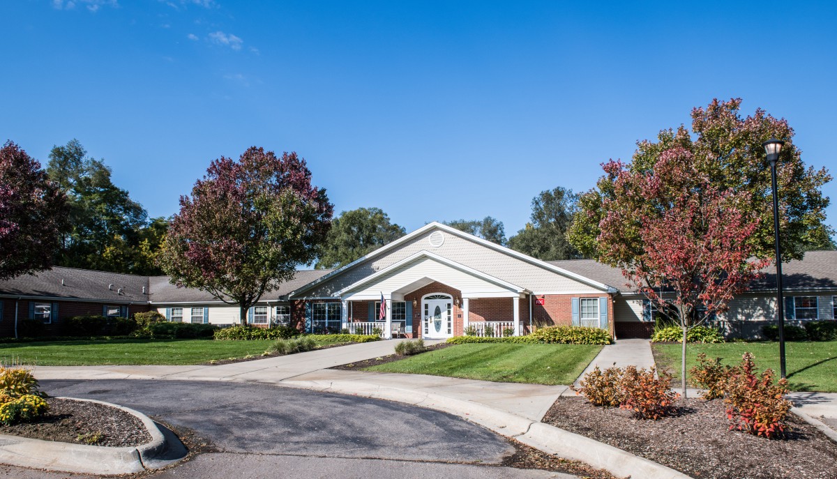 A single-story building surrounded by trees and a well-maintained lawn, with a driveway in front.