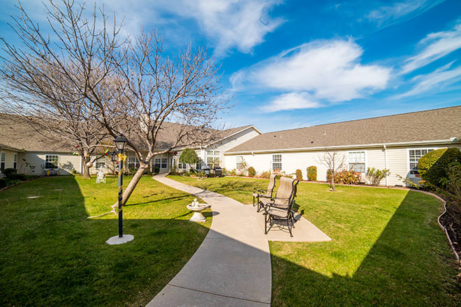 A serene courtyard with a walkway, seating area, and trees under a clear blue sky.