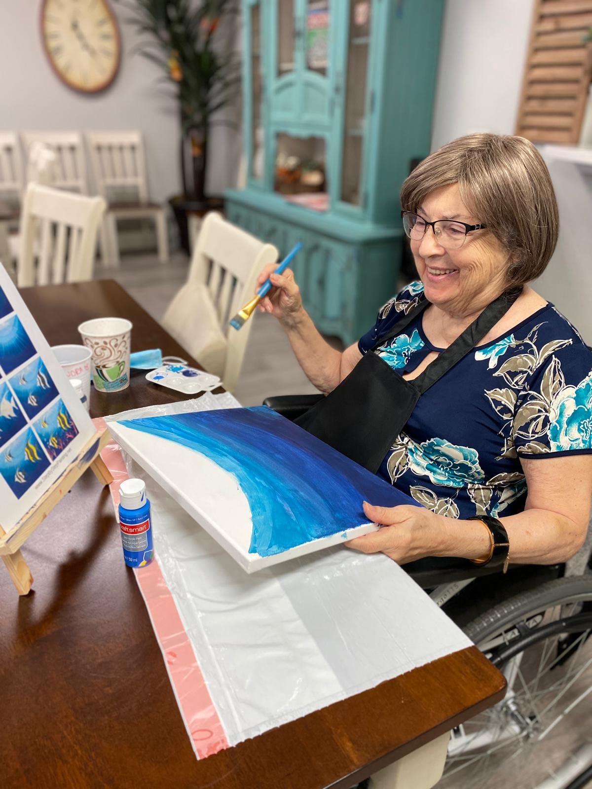 A woman smiling while painting a canvas indoors.