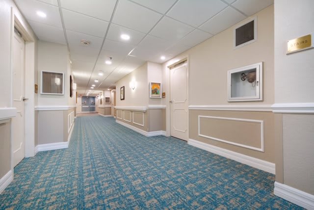 A well-lit hotel hallway with patterned carpet and framed pictures on the walls.