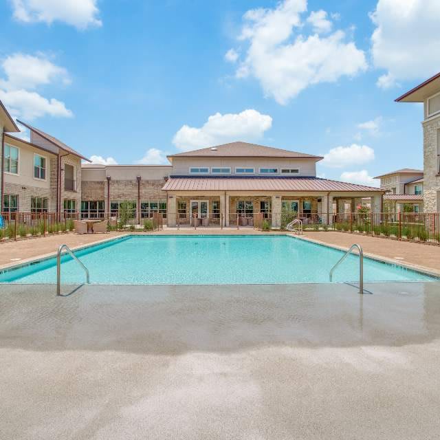 A view of a spacious outdoor swimming pool surrounded by residential buildings under a partly cloudy sky.