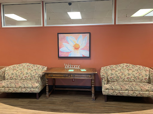 A cozy waiting area featuring floral artwork against an orange wall, complemented by two upholstered chairs and a wooden table.