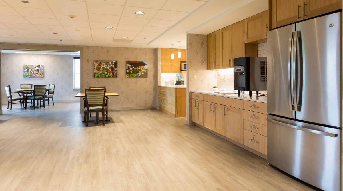 A modern kitchen with wooden cabinets and a small seating area adorned with decorative art on the walls.