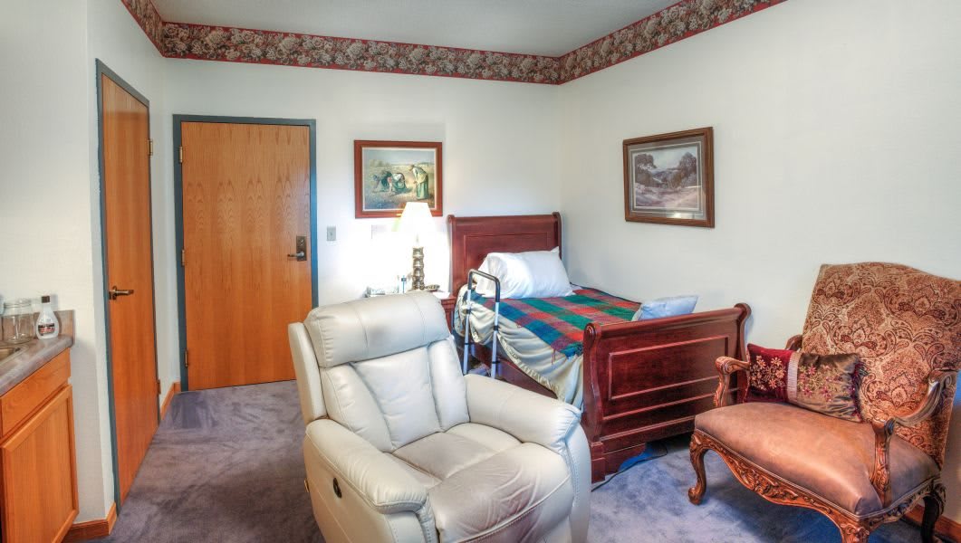 A cozy bedroom featuring a hospital bed, comfortable armchair, and decorative artwork on the walls.