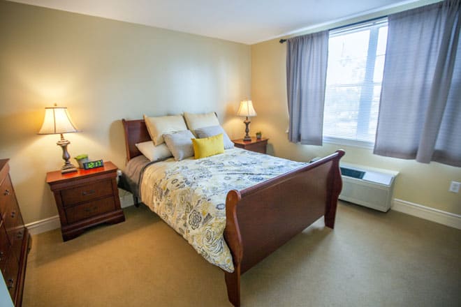 A cozy bedroom with a neatly made bed, wooden furniture, and soft lighting.