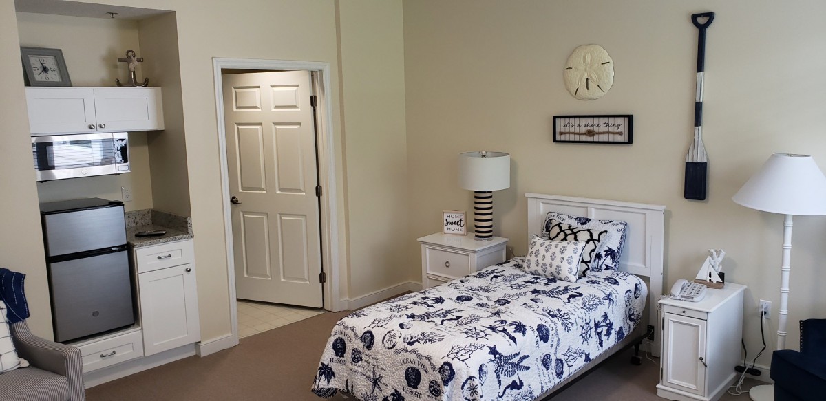 A cozy bedroom with a single bed, nightstand, and decorative lamp beside it. A door is visible to the side.
