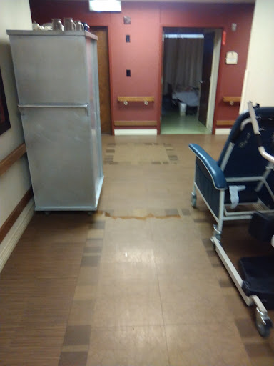 A view of a hospital corridor with a wheelchair and refrigerator.