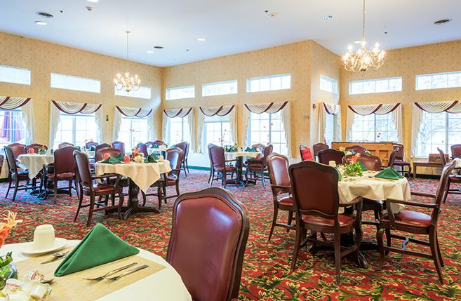 An elegant dining room with neatly arranged tables and comfortable chairs, featuring large windows and chandeliers.