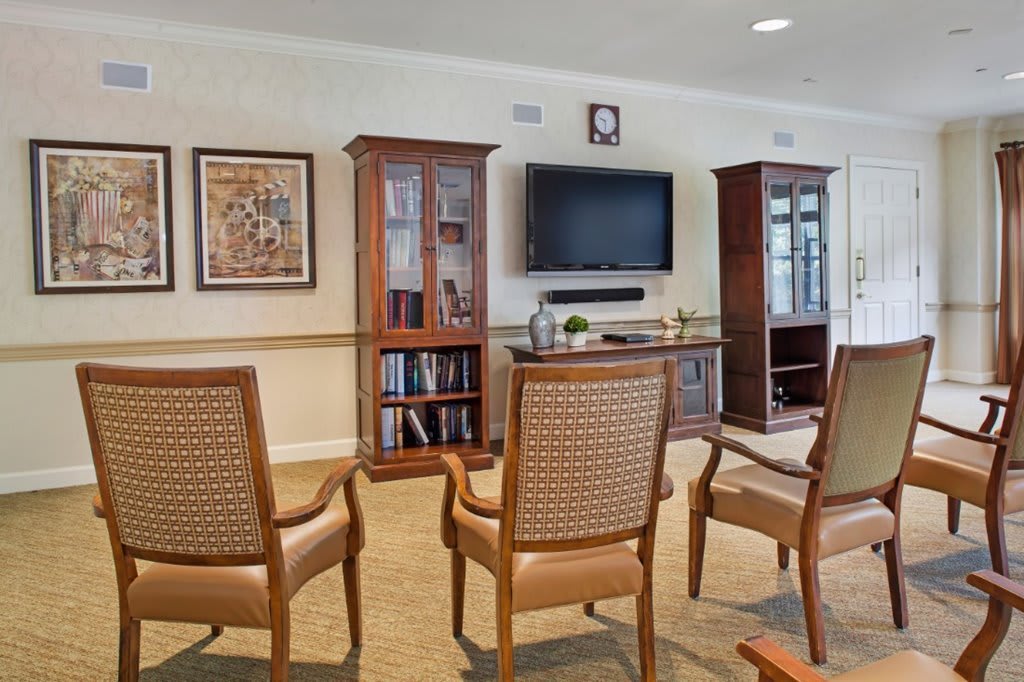 A cozy living room with a seating area, featuring four chairs facing a television mounted on the wall and flanked by cabinets and bookshelves.