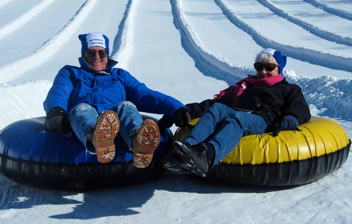 Two people enjoying snow tubing on a winter day.