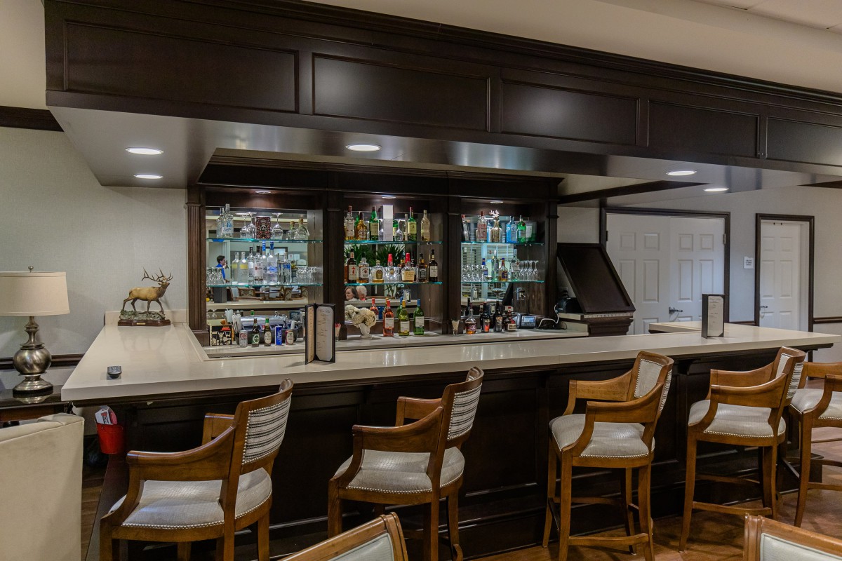 A stylish bar interior with wooden chairs and a well-stocked counter.