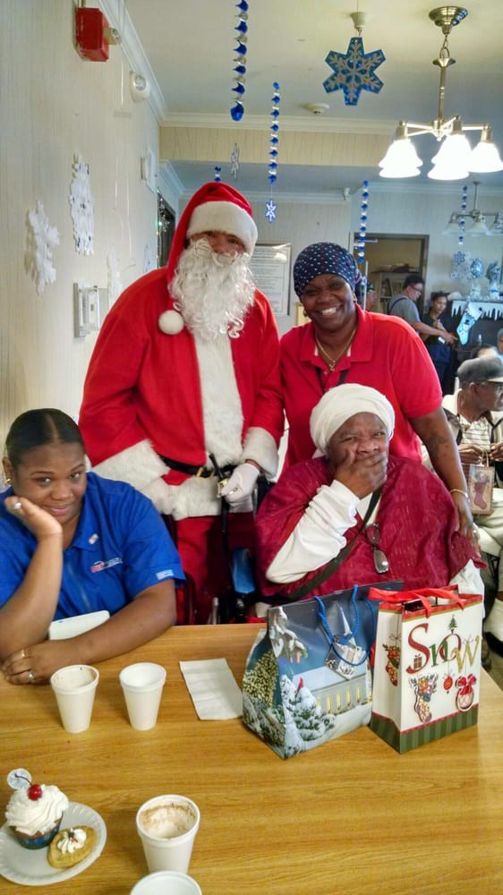 A festive group celebrates Christmas with Santa Claus, surrounded by holiday decorations and gifts.