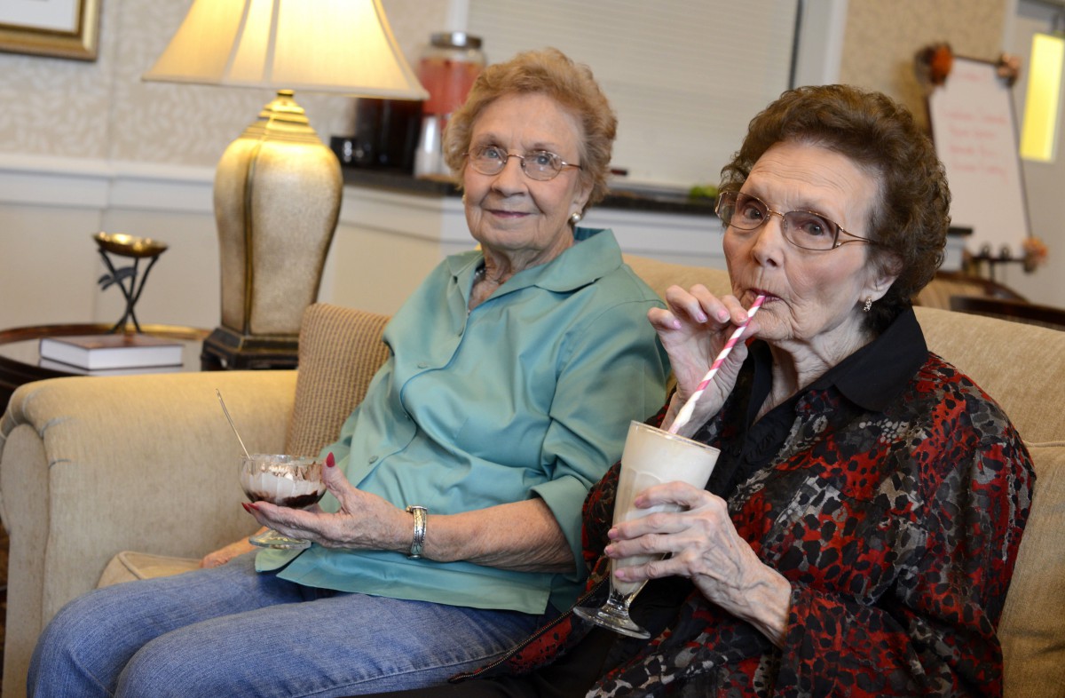 Two elderly women enjoying drinks together indoors.