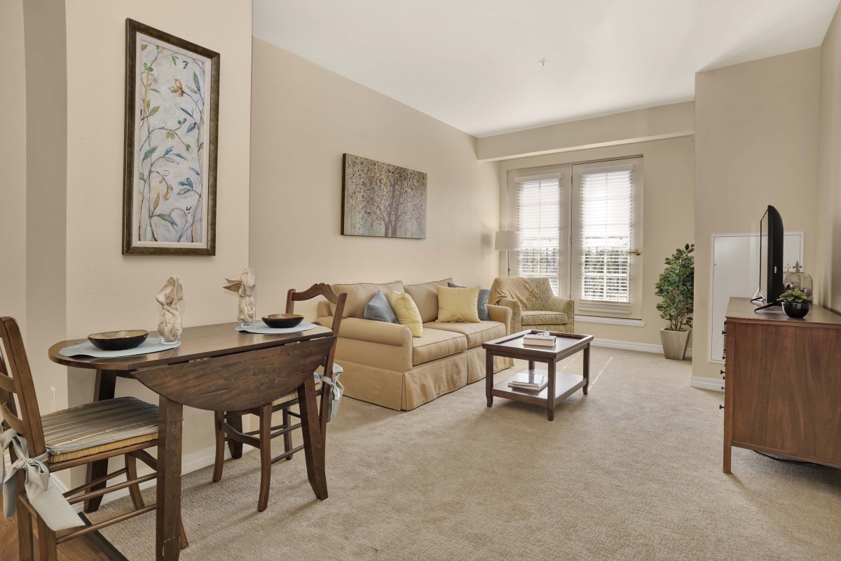 A cozy living room with a dining area, featuring neutral tones and comfortable furniture.