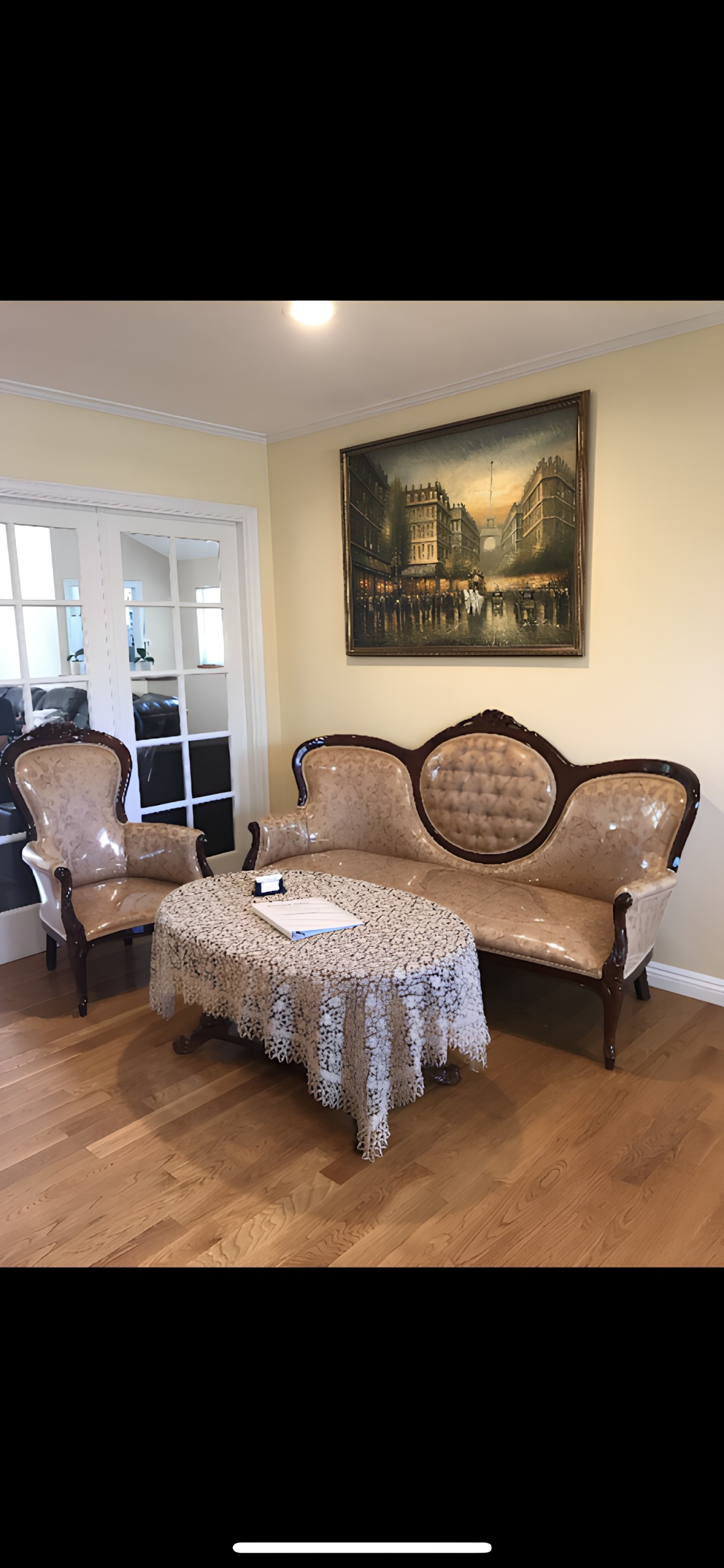 A cozy living room featuring vintage furniture including an antique sofa and armchair, complemented by a lace-covered coffee table and elegant wall art.