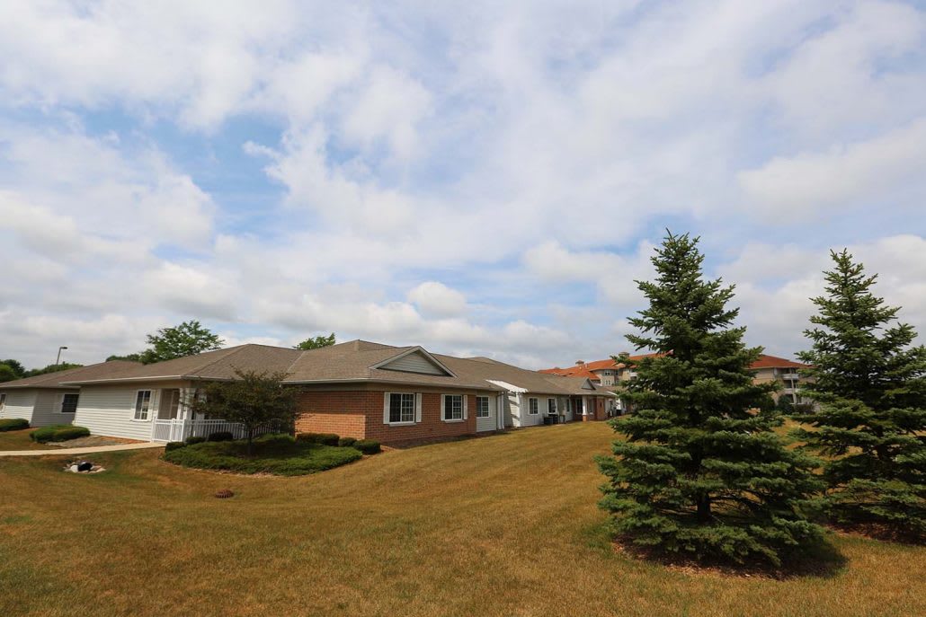 A single-story house with a well-manicured lawn and a tree under a cloudy sky.