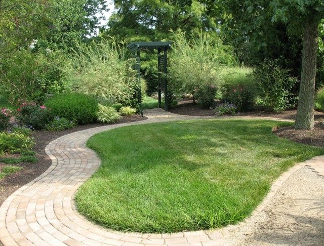 A beautifully landscaped garden with a curved pathway, lush green lawn, and an archway leading to a secluded area.