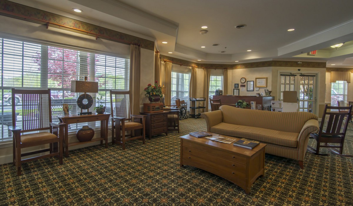 A cozy and elegantly furnished living room with a large couch, wooden tables, and ample natural lighting.