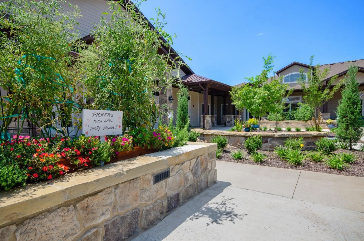 A beautifully landscaped garden with a stone wall and vibrant flowers, leading up to a house on a sunny day.