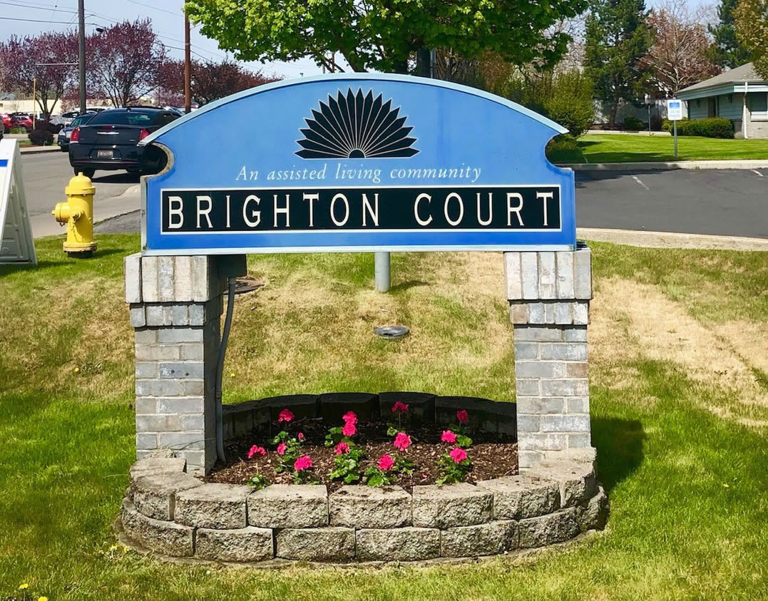 A welcoming sign for Brighton Court surrounded by greenery and flowers.