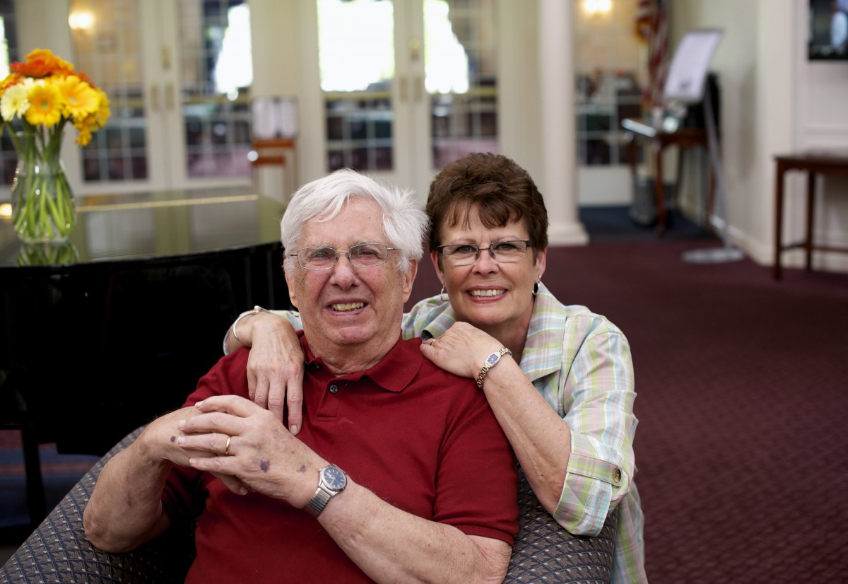 An elderly couple smiling and embracing indoors.