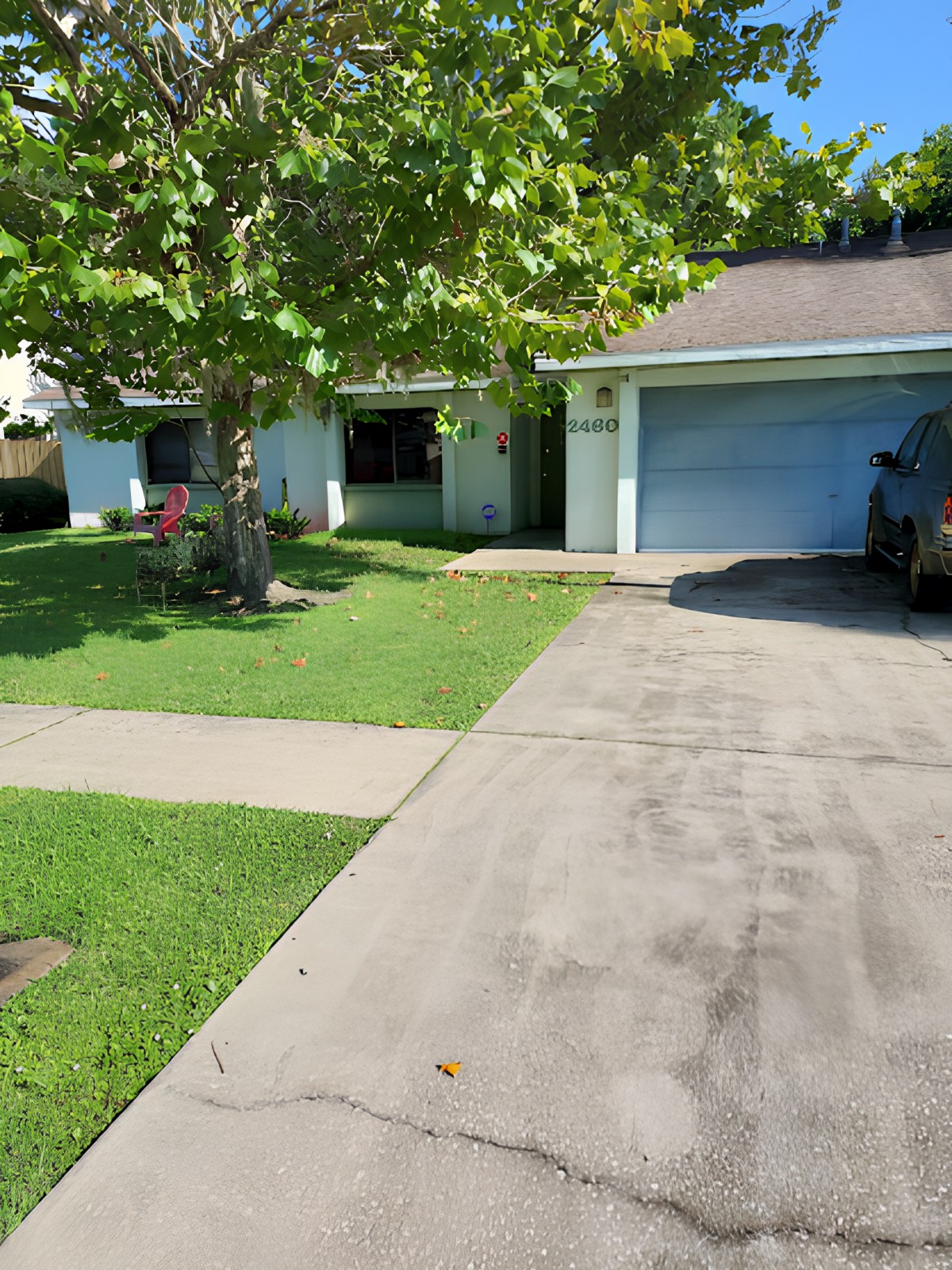 A suburban house with a tree and driveway leading to a garage.