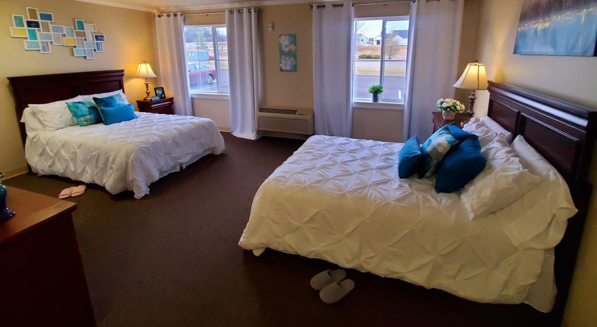 A cozy bedroom with two beds, decorated with curtains and lamps, featuring a carpeted floor and windows for natural light.